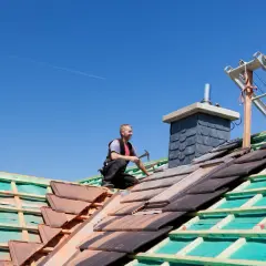 Ceglany dach w trakcie budowy, robotnik kładzie dachówki.